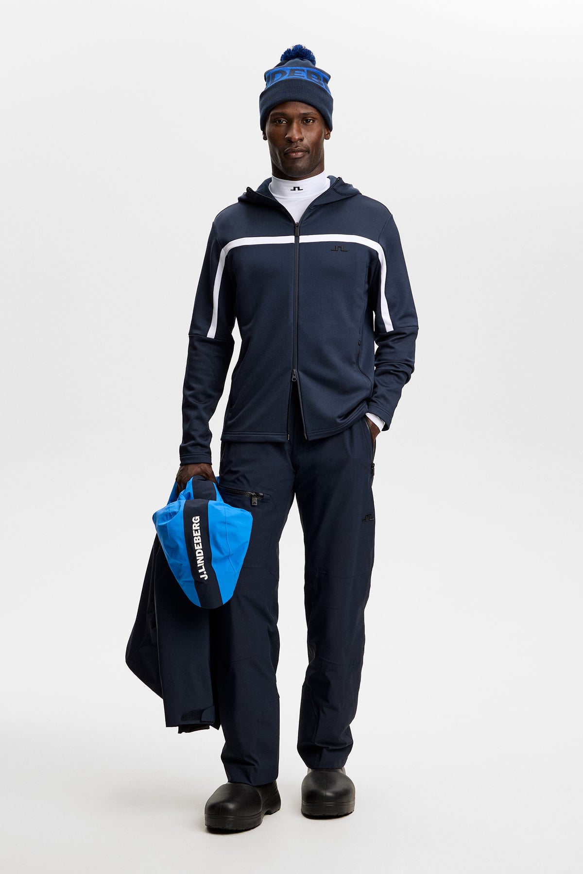 Sett forfra: Sharpe Full Zip Hood i JL Navy på modell i et studio, med hvit bryststripe og Bridge-logo.