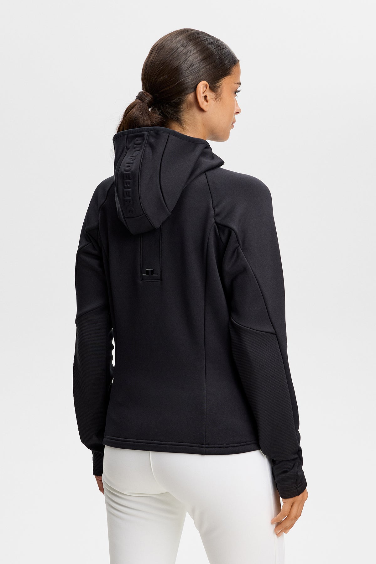 Set bagfra: Sort Portia Polartec Hood med præget J.LINDEBERG-logo på hætten og Bridge-logo på ryggen.