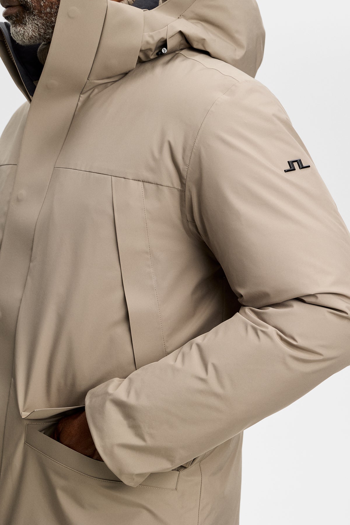 Close-up: Alon Down Parka in Brindle met Bridge-logo op de mouw, steekzak en capuchondetail.