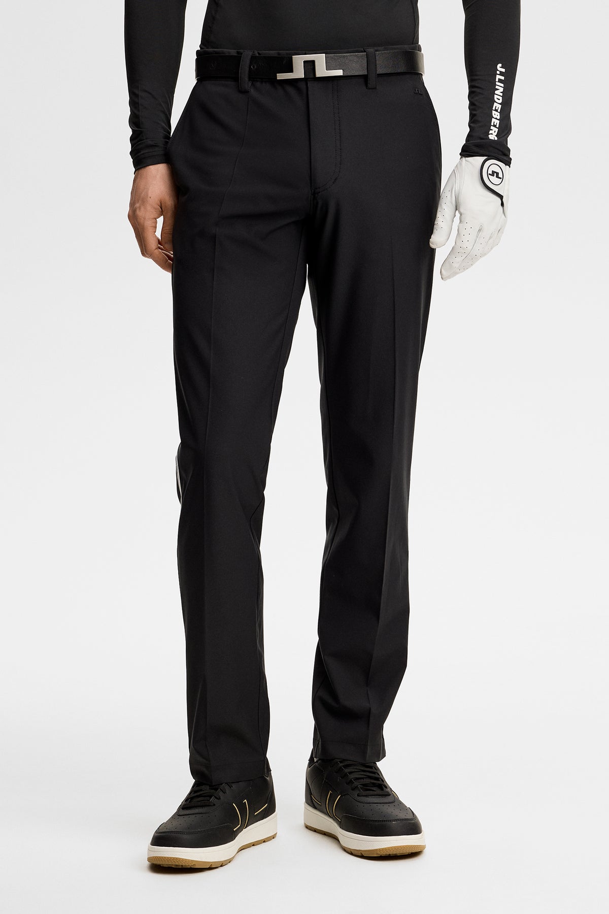 Vorderansicht: Schwarze Mitch Stripe Pant am Model, kombiniert mit Bridge-Logo-Gürtel und weißem Golfhandschuh.