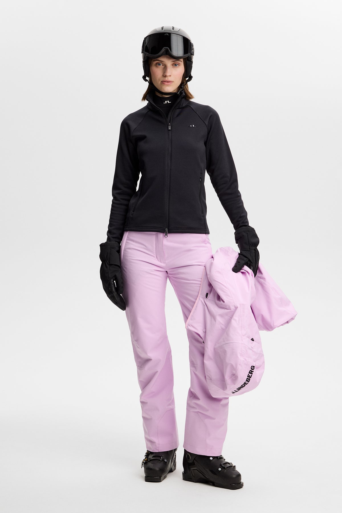 Vorderansicht: Schwarzer Portia Polartec Mid Layer an einem Model, kombiniert mit rosa Skihose und Helm.