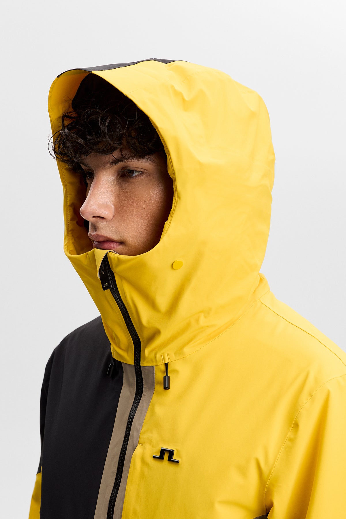 Nærbillede: Caldwell Jacket i Bumblebee med hætte oppe, høj krave og Bridge-logo på brystet.