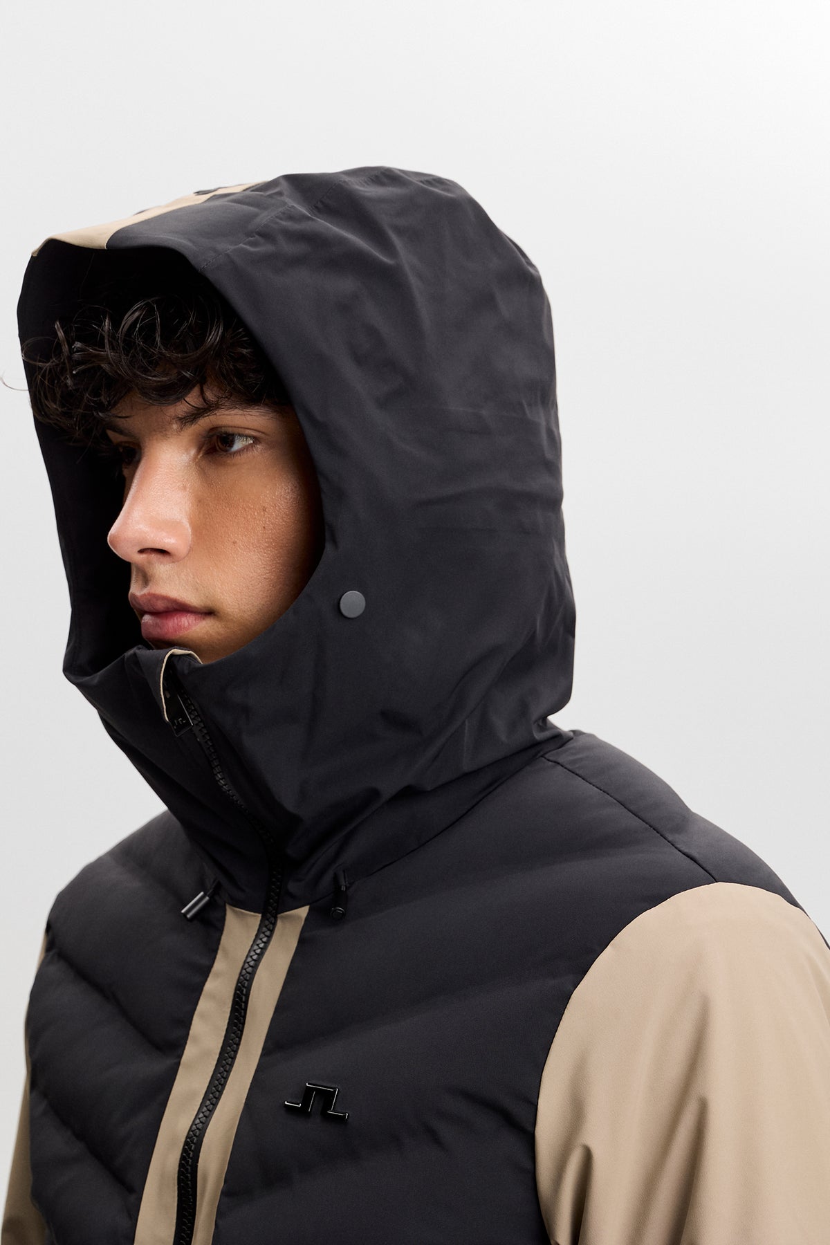 Nærbillede: Blackwell Jacket i Brindle med hætten oppe, høj krave og Bridge-logo på brystet.