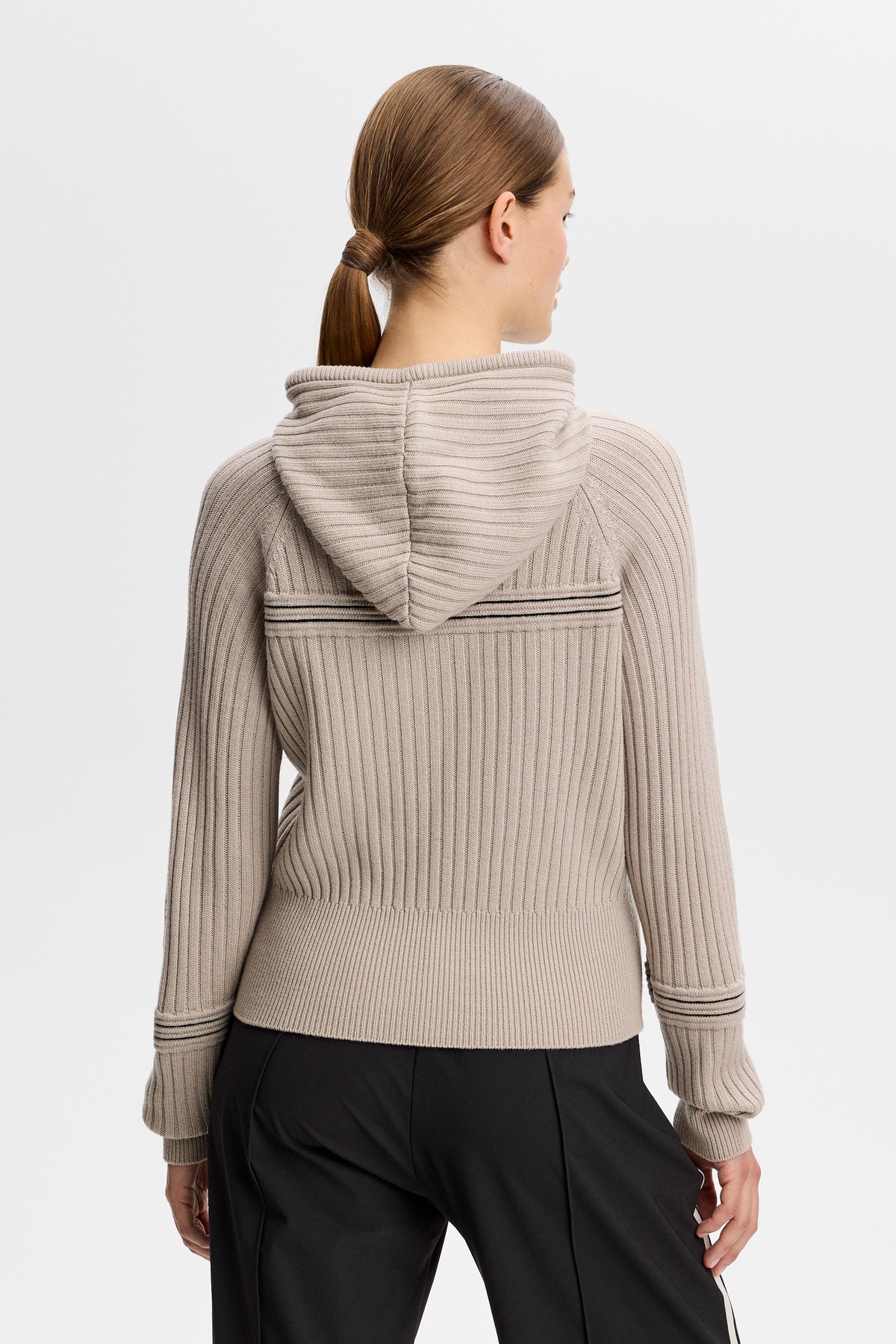 Rückansicht: Hilda Knitted Rib Hoodie in Moonbeam mit gestrickter Kapuze und Rippstruktur, getragen zu einer schwarzen Hose.