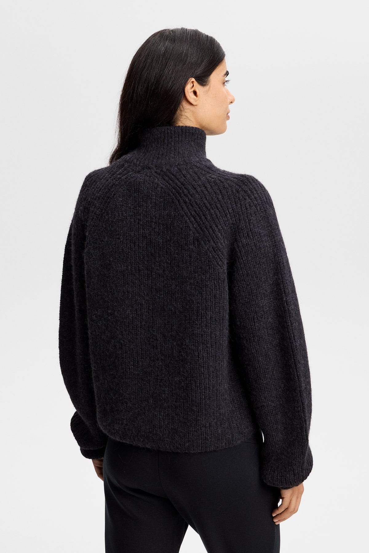 Sett bakfra: Svart Whitney Rib Knit Full Zip med grov ribbestrikk, raglanermer og høy krage, på modell i studio.