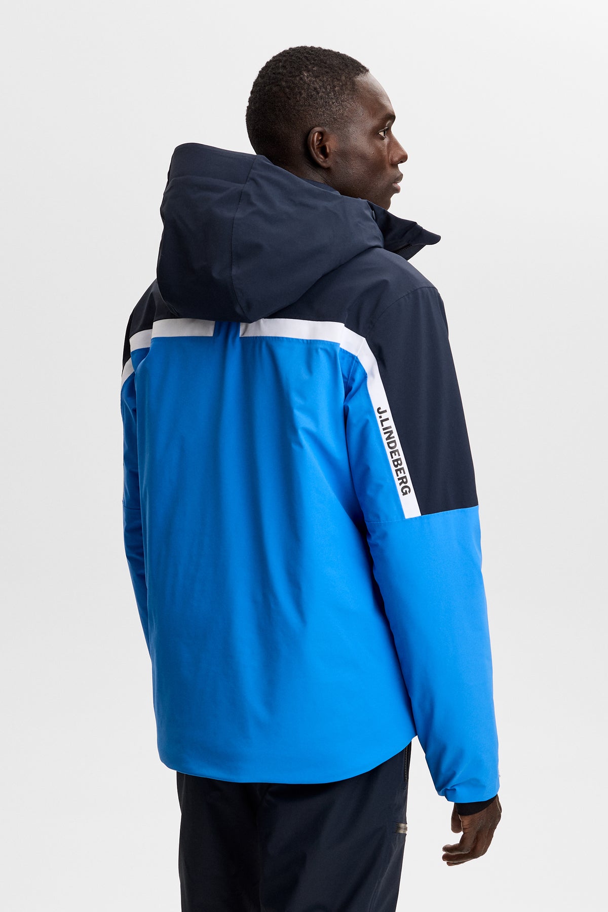 Back view: Windsor Jacket in Sonic Blue with color-block panels, hood, and J.LINDEBERG sleeve logo.