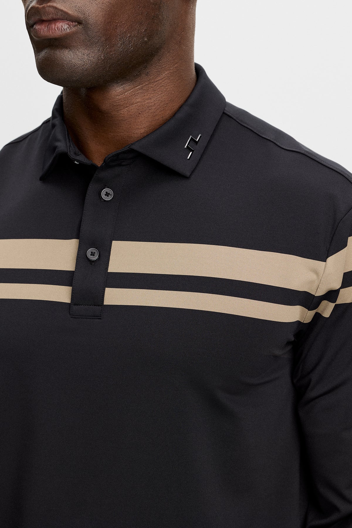 Close-up of the black Kenny LS stripe polo showing the button placket, beige chest stripes, and Bridge logo on the collar.