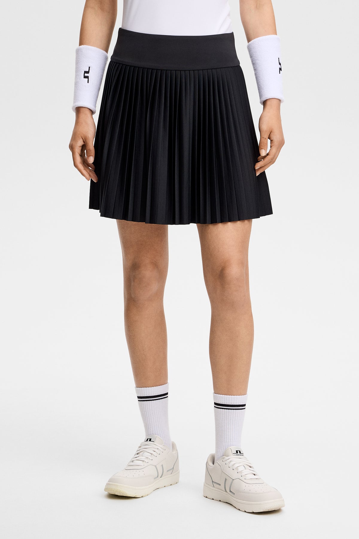 Vooraanzicht: Model draagt de zwarte Alexandra Skirt met geplooide zoom en brede tailleband.