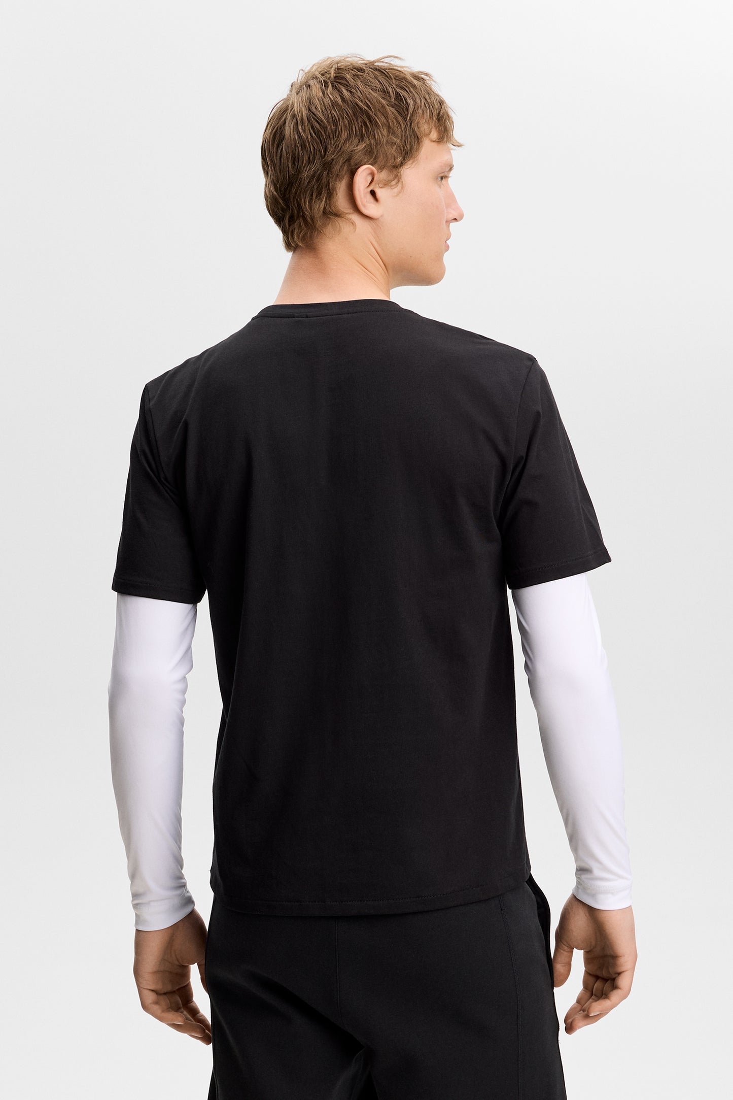 Back view: Black Alpha Graphic T-shirt worn by a model layered over a white long-sleeve top.