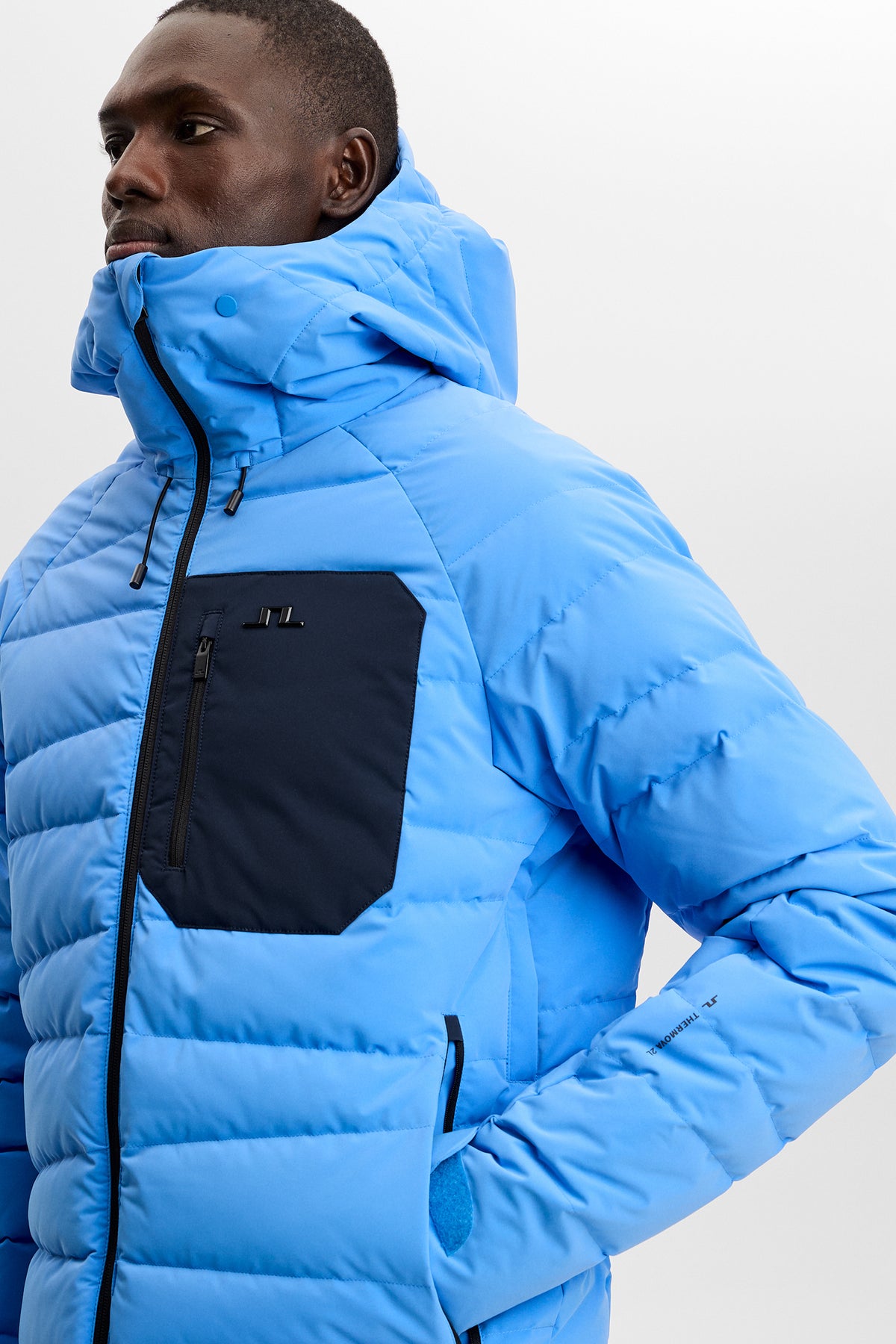 Close-up view: Thornton Down Jacket in Sonic Blue with contrasting chest pocket, hood, and Bridge logo.