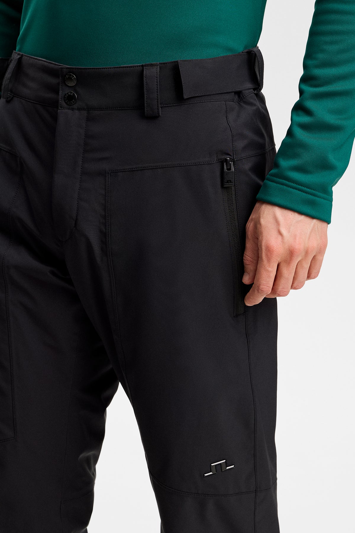 Detailansicht: Schwarze Clarke Pant mit Reißverschlusstasche, Gürtelschlaufen und Bridge-Logo am Bein.