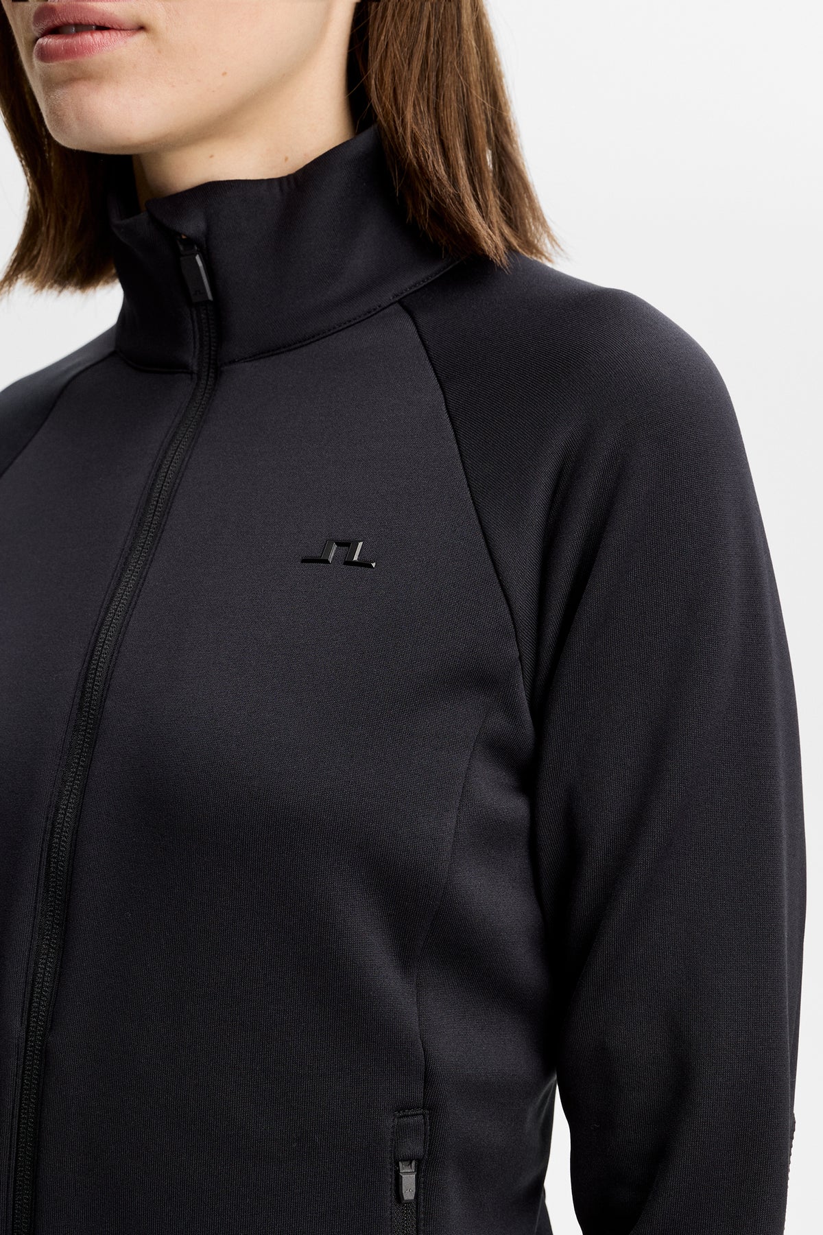 Detailansicht: Portia Polartec Mid Layer in Schwarz mit hohem Kragen, Reißverschluss und Bridge-Logo auf der Brust.