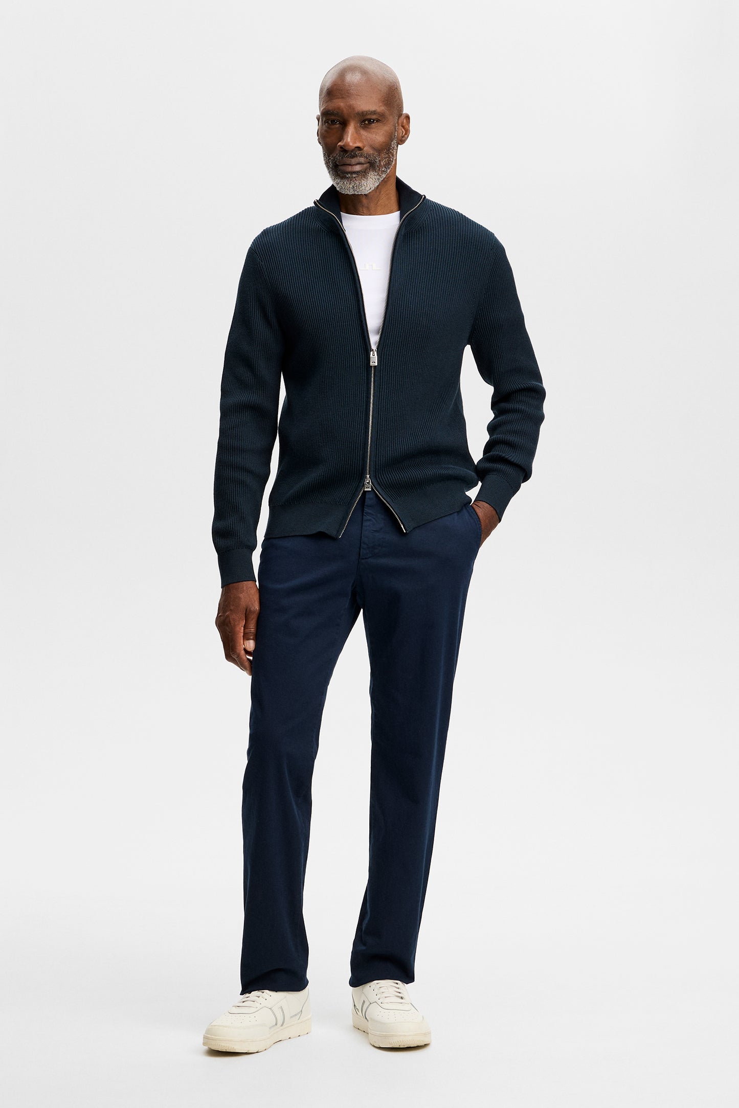 Vue de face : Chaze Cotton Stretch Pants GD en JL Navy porté avec un gilet zippé en maille et des baskets blanches.