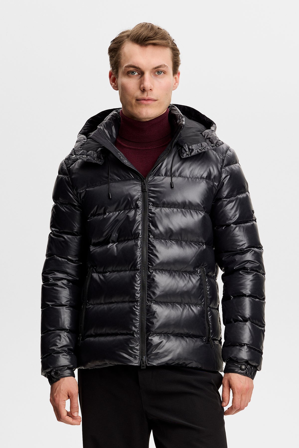 Vorderansicht: Schwarze Creek Light Down Jacket mit glänzender Steppung und Kapuze an einem Model.