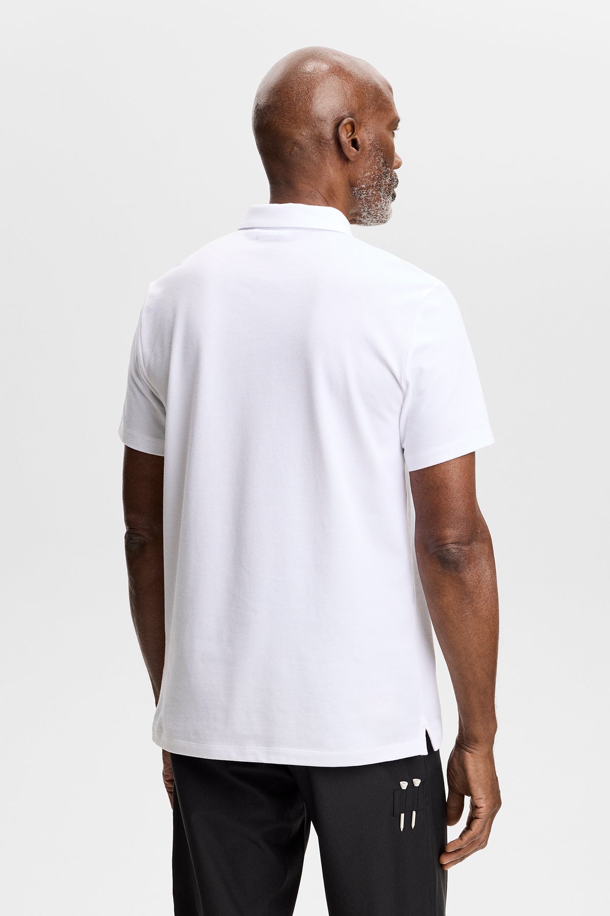Achteraanzicht: Model draagt de witte Verse Button Down Polo met korte mouwen op een zwarte golfbroek.