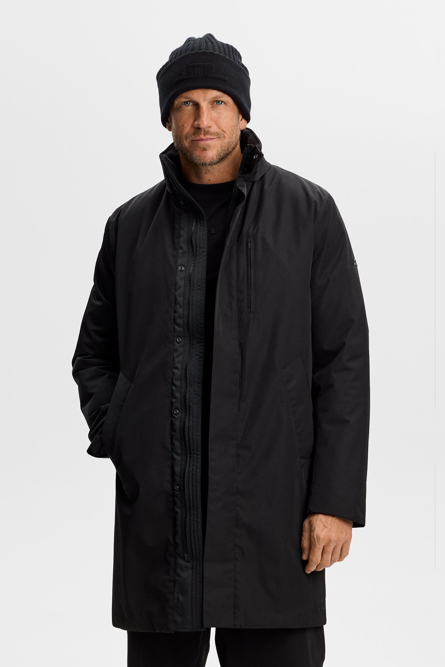 Harold Padded Jacket in black, front view on a model, featuring an open zip closure, ribbed collar, and chest pocket.