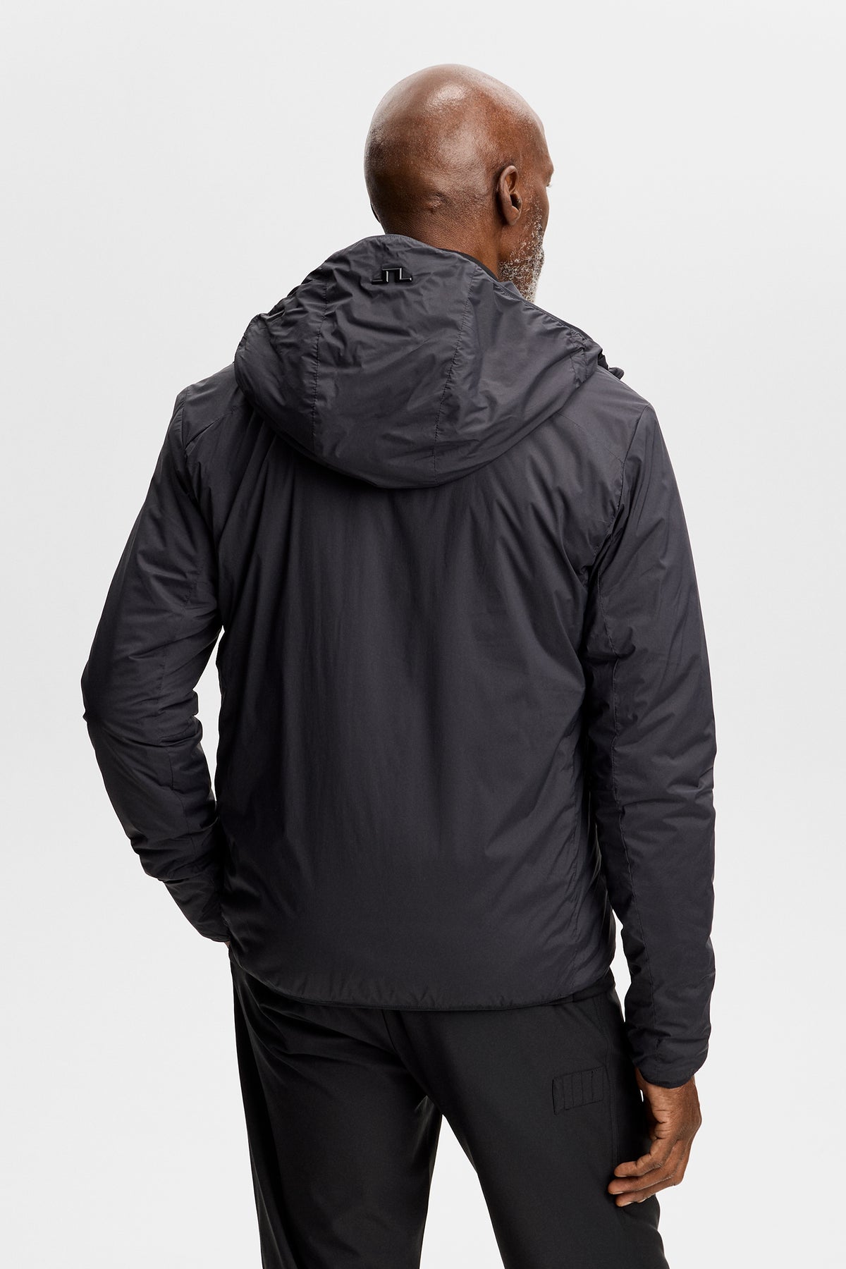 Back view: Clinton Hood jacket in black featuring an attached hood with Bridge logo detail.