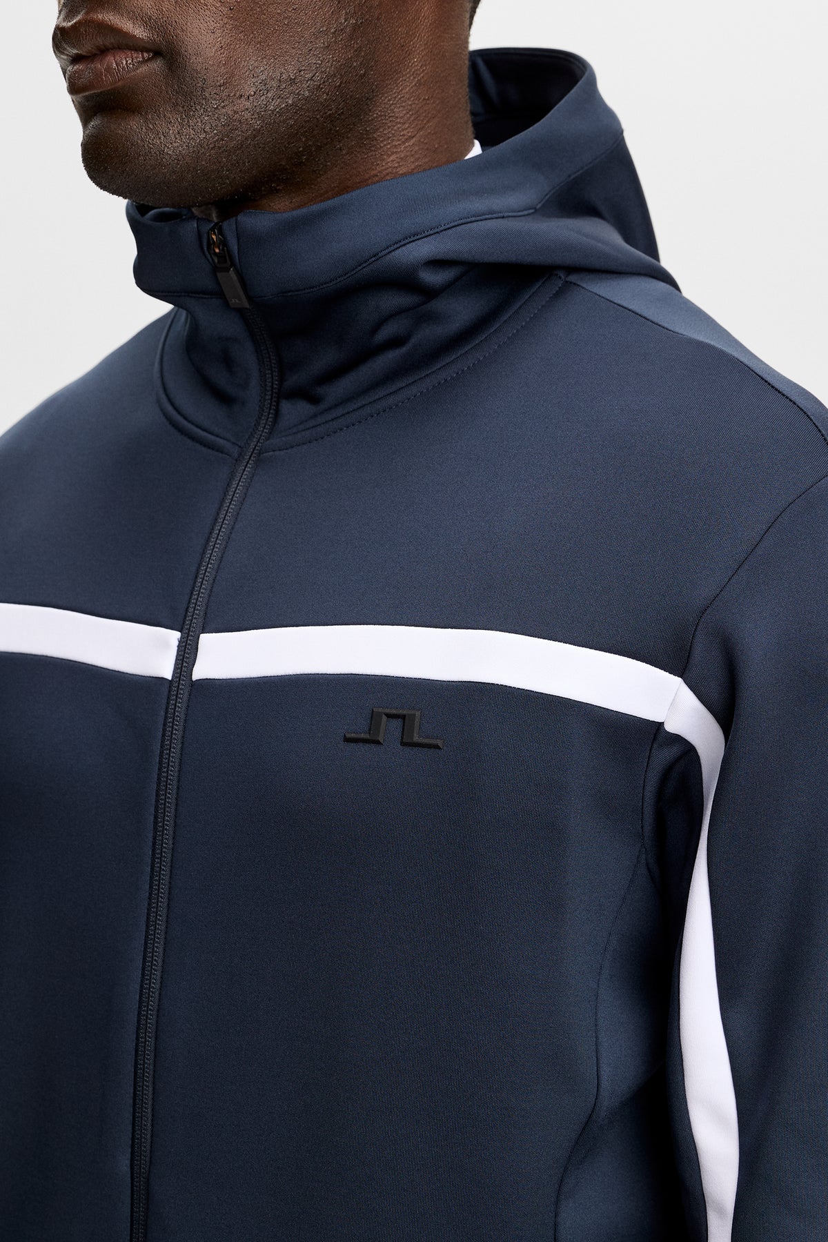Nærbilde: JL Navy Sharpe Full Zip Hood med hette, glidelås, hvit kontraststripe og Bridge-logo på brystet.
