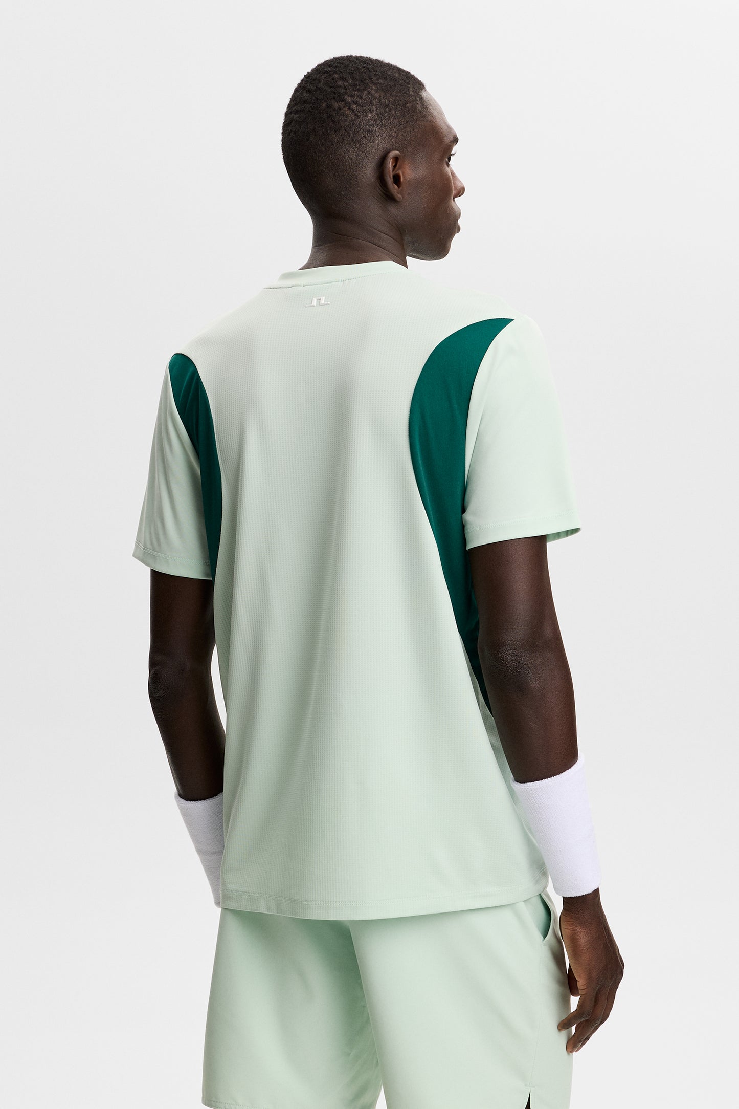 Dennis T-shirt in light green, back view with dark green side panels and a small Bridge logo at the neck.