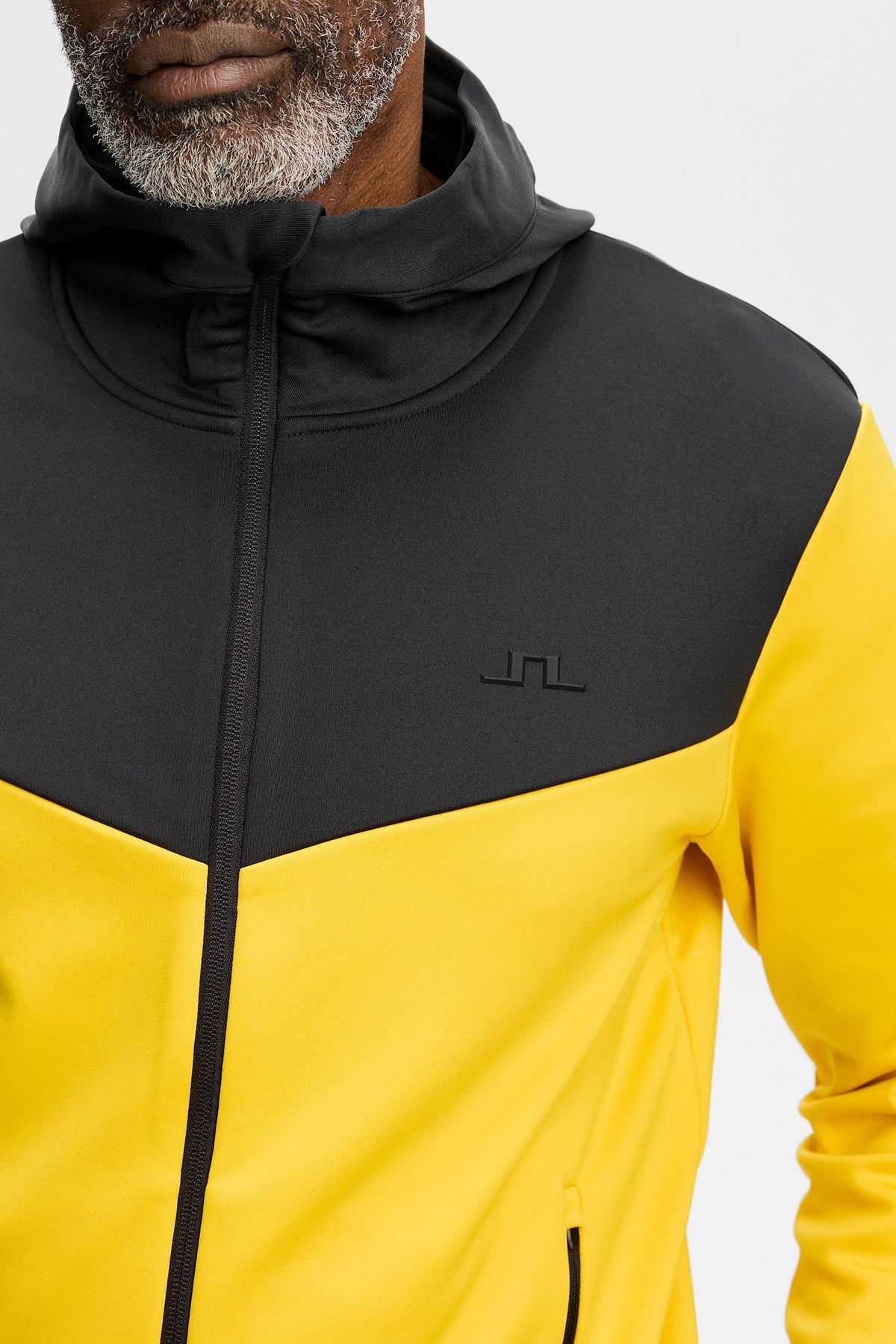 Nærbillede: Maclean Zip Hood i gul og sort med hætte, gennemgående lynlås og Bridge-logo på brystet.