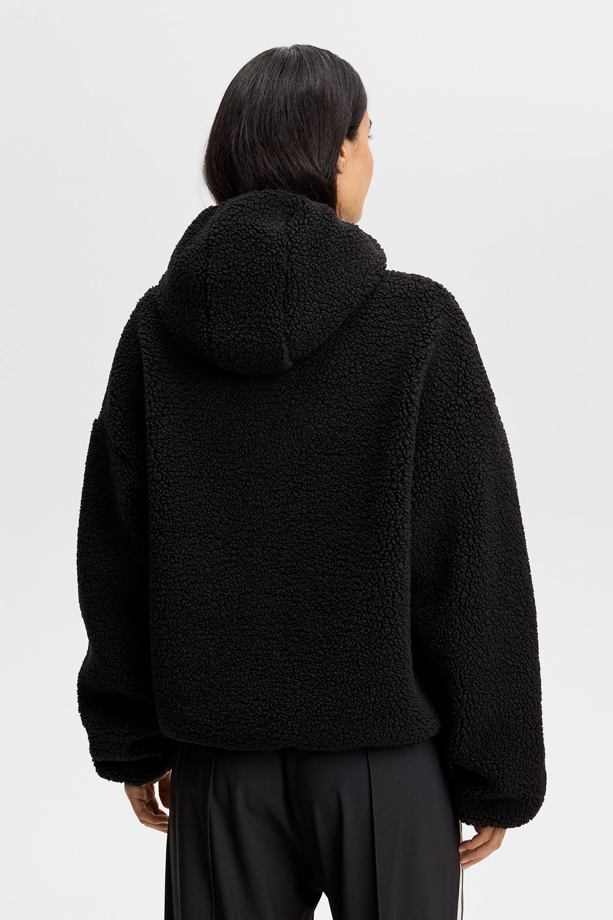 Rückansicht: Schwarzer Comona Pile Hood aus Teddy-Fleece mit fester Kapuze und elastischen Bündchen.