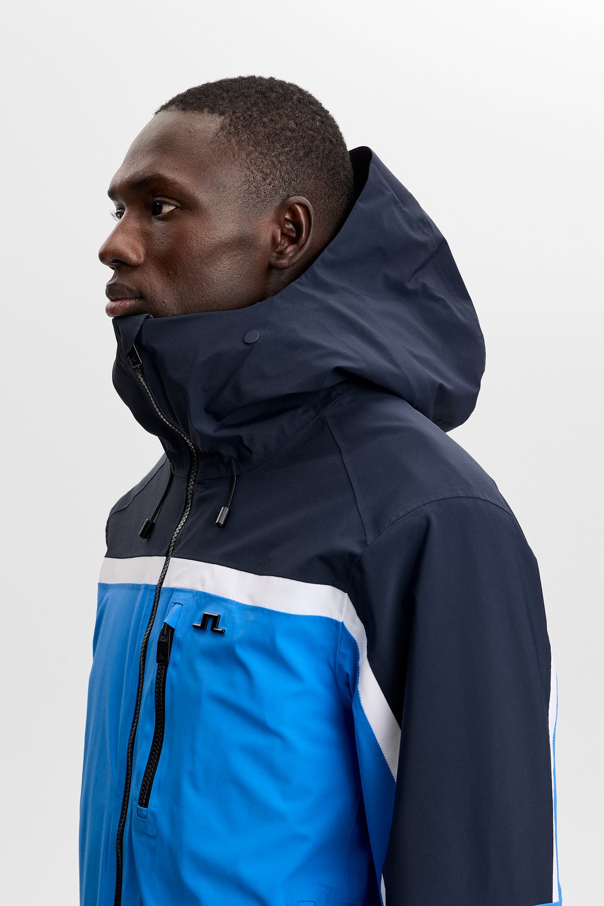 Side view: Windsor Jacket in Sonic Blue with color-blocked panels, high collar, and Bridge logo.