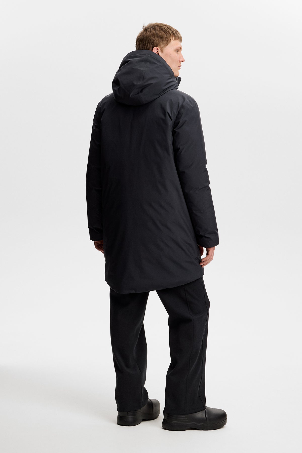 Achteraanzicht: Model draagt de zwarte Alon Down Parka met capuchon en een zwarte broek.