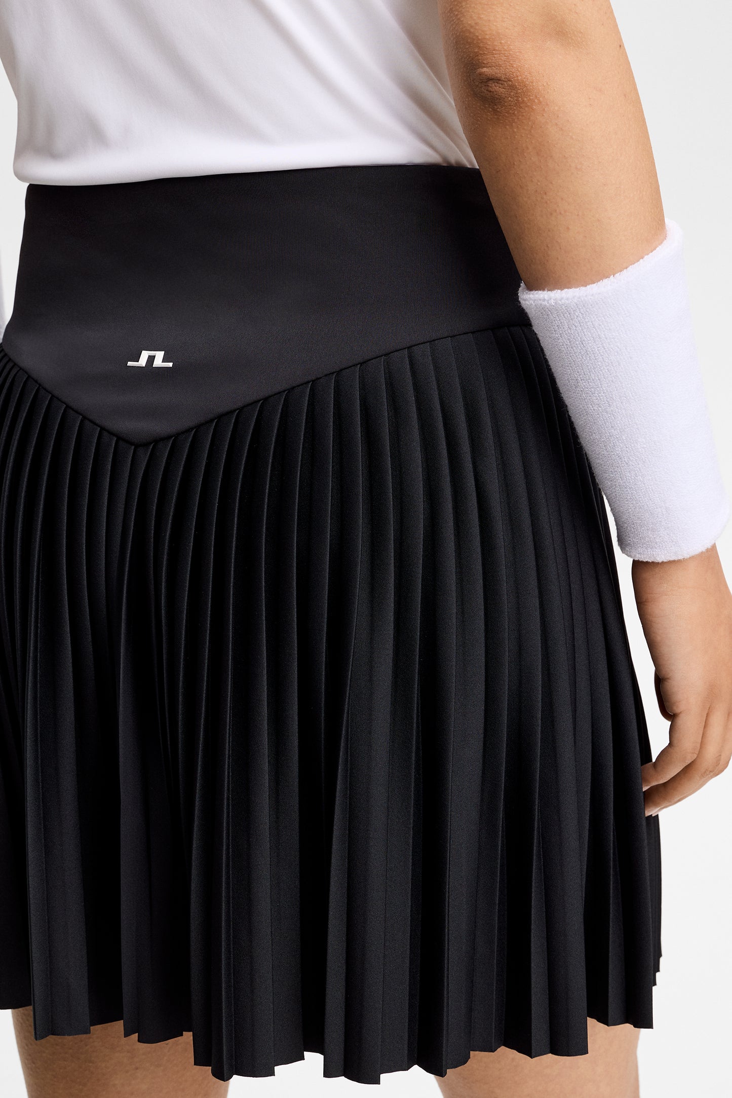 Close-up achterkant: Zwarte Alexandra Skirt met geplooide zoom en Bridge-logo op de tailleband.