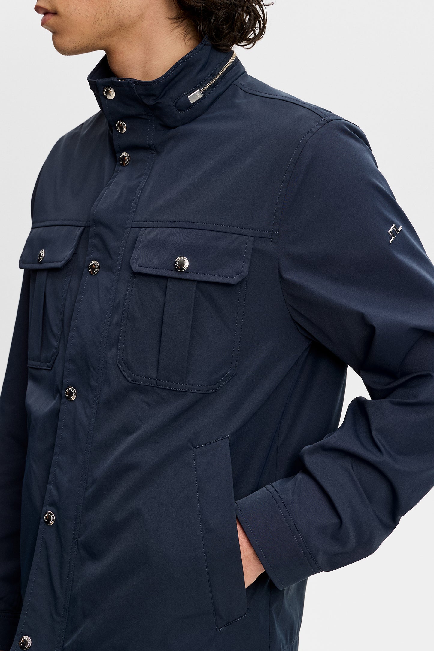 Close-up of the Bailey Recy Poly Jacket in JL Navy featuring flap chest pockets and Bridge logo on the sleeve.