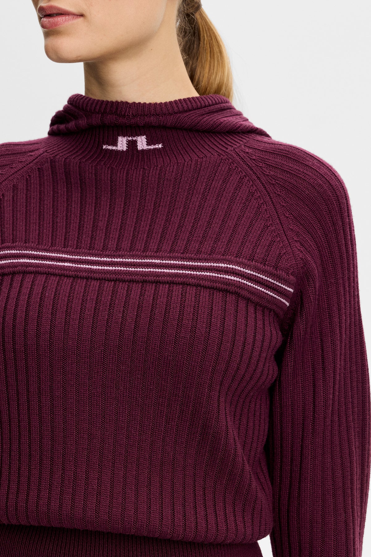 Närbild framifrån: Hilda Knitted Rib Hoodie i Winetasting med stickad Bridge-logotyp vid kragen och ribbad struktur.