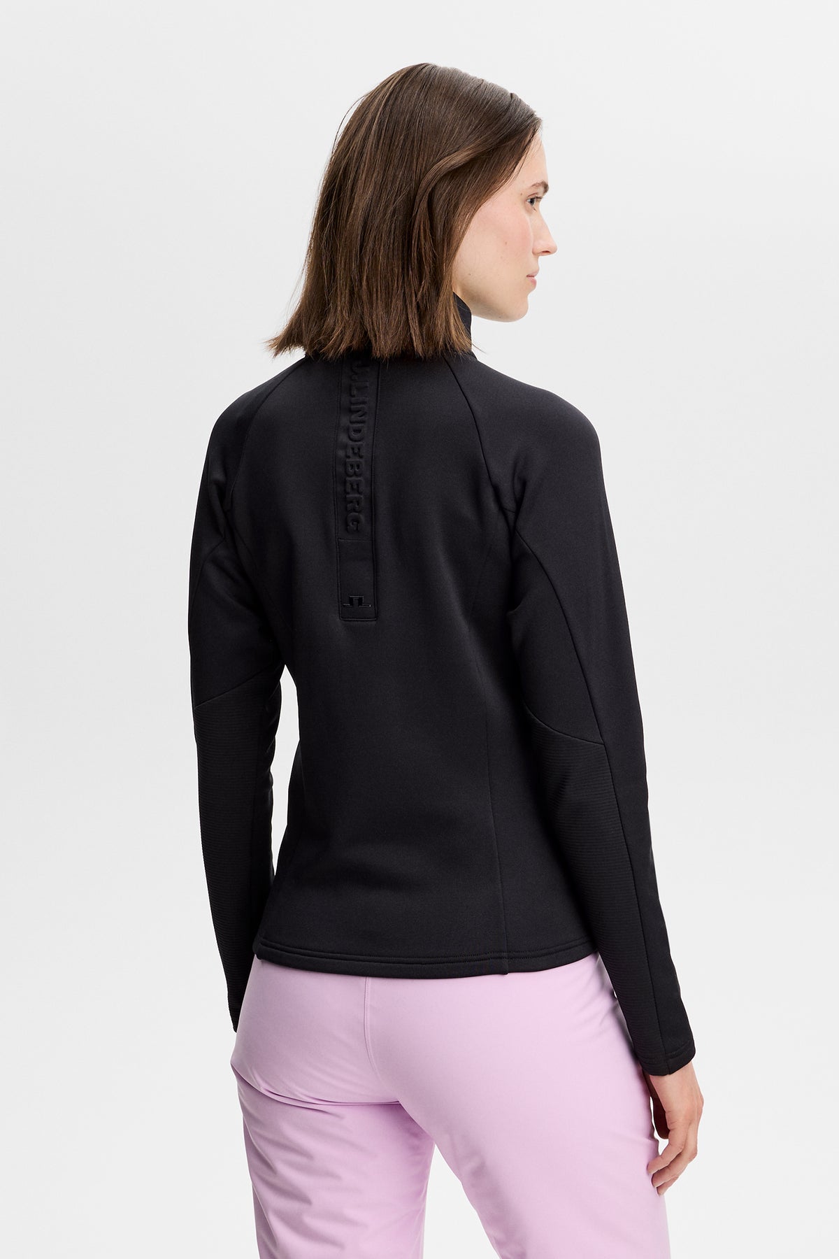 Rückansicht: Portia Polartec Mid Layer in Schwarz mit hohem Kragen und geprägtem J.LINDEBERG-Logo am Rücken.