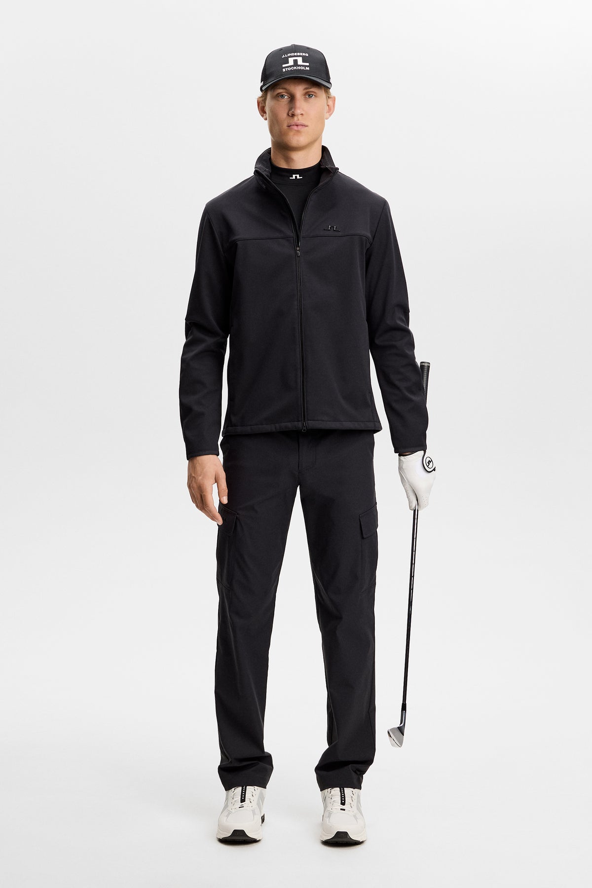 Set forfra: Model i sort Logan Cargo pant med sidelommer, der holder en golfkølle i et studie.