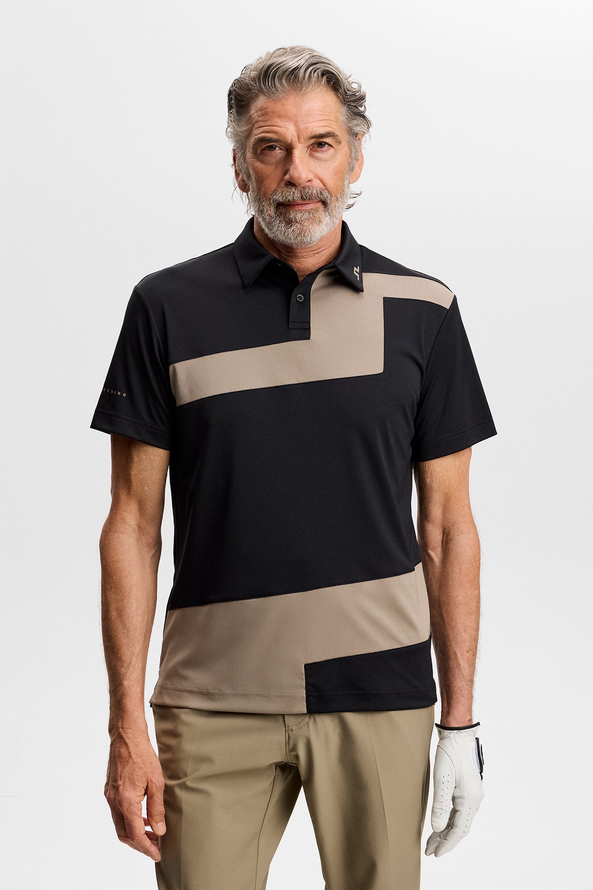 Model wearing the black Sidd Polo with beige contrast front panels, polo collar, and a golf glove in a studio.