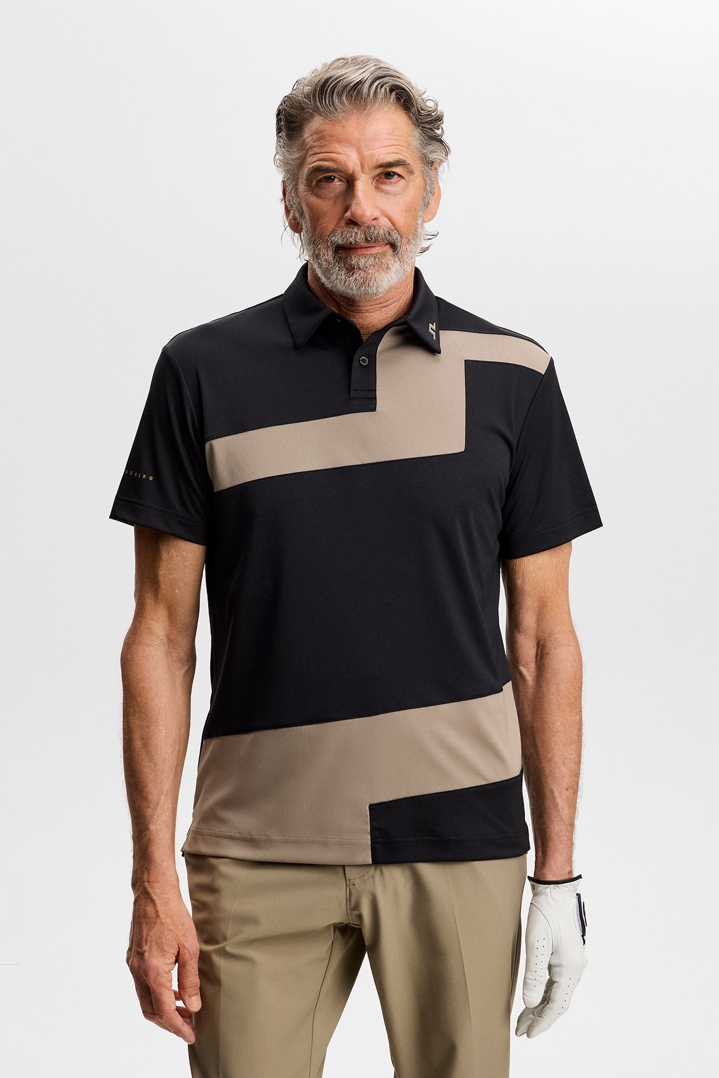 Model wearing the black Sidd Polo with beige contrast front panels, polo collar, and a golf glove in a studio.