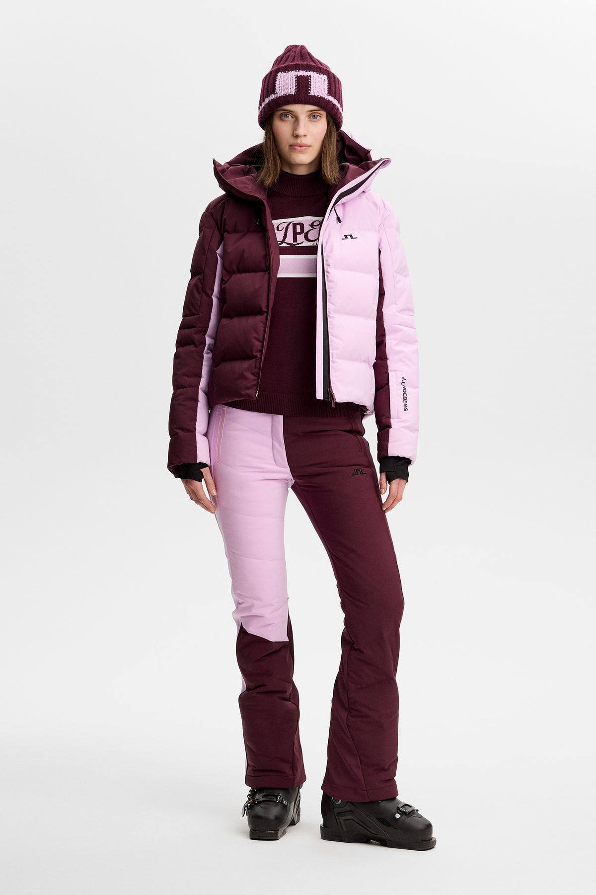 Vorderansicht: Nerina Blocked Down Jacket in Winetasting an einem Model, kombiniert mit Skihose und Beanie.