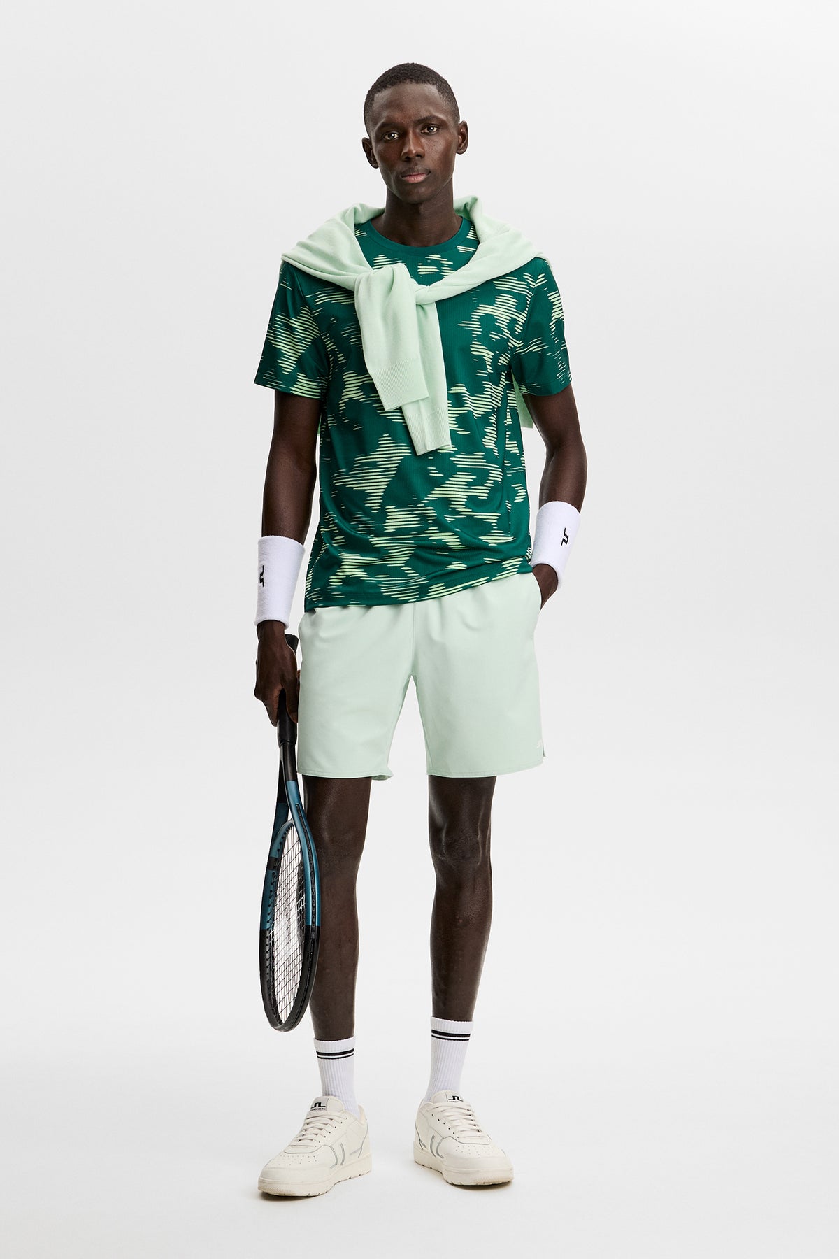 Vorderansicht: Grünes Josip Printed T-Shirt mit Allover-Muster an einem Model mit hellgrünen Shorts und Tennisschläger.