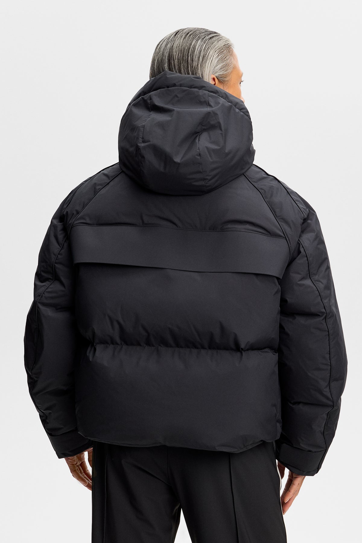 Achteraanzicht: Model draagt de zwarte Lea Down Jacket met capuchon en gewatteerde kamers.