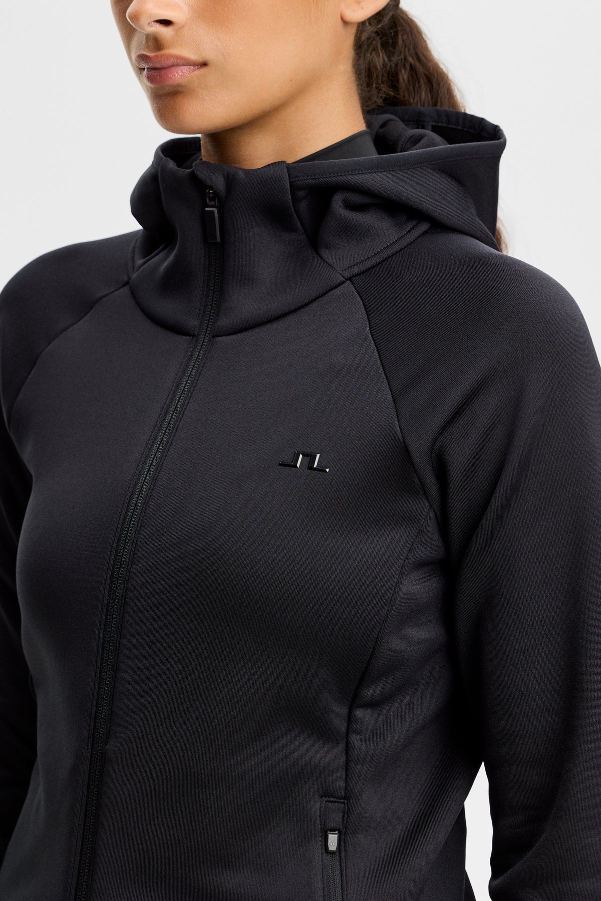 Nærbillede: Sort Portia Polartec Hood med hætte, høj hals, lynlås foran og Bridge-logo på brystet.
