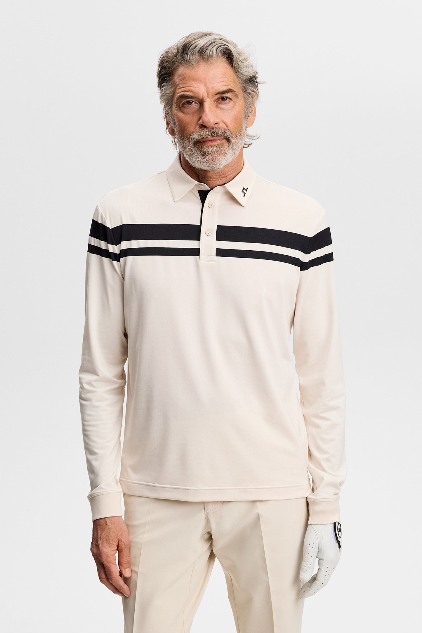 Model wearing the beige Kenny LS stripe polo with black chest stripes, polo collar, and a golf glove in a studio setting.