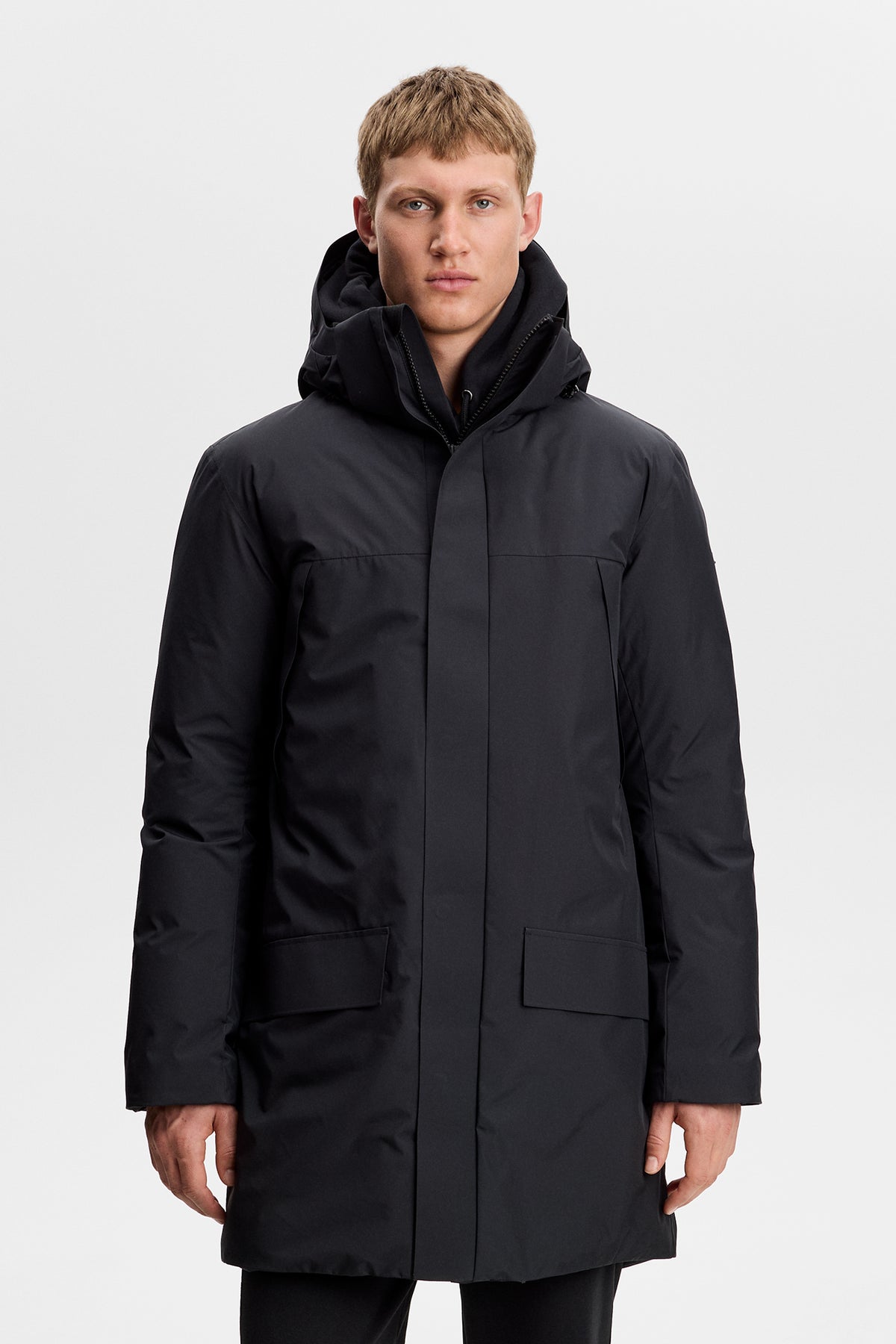 Vooraanzicht: Model draagt de zwarte Alon Down Parka met capuchon en klepzakken aan de voorkant.
